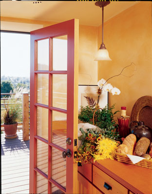 The remodeled kitchen opens onto the new deck via a salvaged French door. Kitchen cabinets, made by Tom Harrison of Alter-Eco, are of wheatboard; cabinet doors and drawer fronts are of reclaimed Douglas fir (note the character marks from old iron-nail stains). The countertop is Richlite, a durable composite of wood fiber and resin. The walls have a coat of gypsum plaster over sheetrock, and the final coat is a translucent casein glaze tinted with mineral pigment.